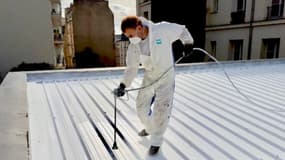 Un homme en train de repeindre une toiture en blanc.