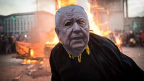 Un participant au carnaval de Marseille affublé d'un masque de Jean-Claude Gaudin, le maire de la ville, pose devant une statut de ce dernier à laquelle il a été mis le feu, le 10 mars 2019
