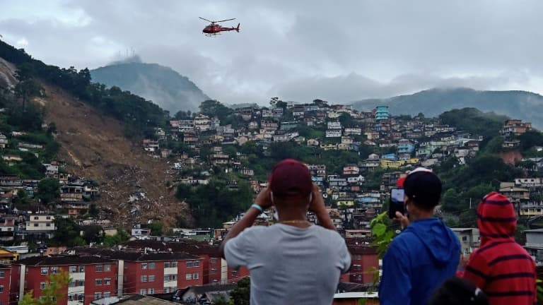Des habitants observent un hélicoptère des services de secours survolant un grand glissement de terrain à Petropolis (Brésil), le 18 février 2022.