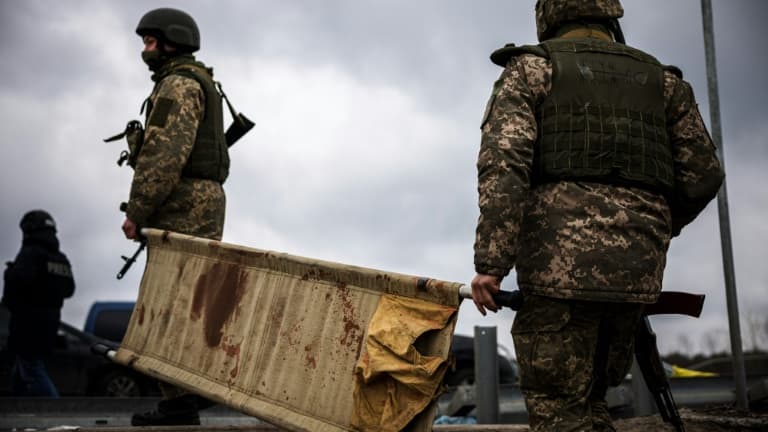Des soldats ukrainiens transportent une civière ensanglantée, à Irpin, au nord-ouest de Kiev, le 13 mars 2022