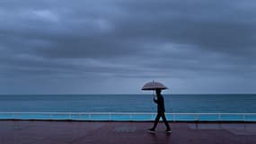 Un passant s'abrite de la pluie sous un parapluie, le long de la plage sur la "Promenade des Anglais" à Nice, le 30 octobre 2023. Photo d'illustration