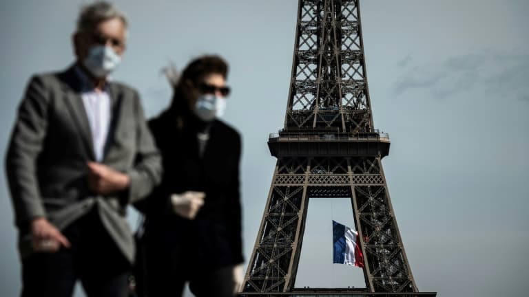 Homme et femme portant un masque devant la Tour Eiffel à Paris. 