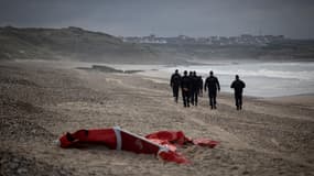 Des policiers français patrouillant sur la plage entre Ambleteusse et Wimereux, dans le nord de la France, passent devant l'épave d'un bateau pneumatique utilisé par des migrants qui tentent de traverser la Manche vers l'Angleterre, le 16 octobre 2021. 