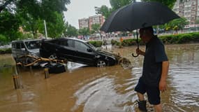 Un homme passe devant une voiture endommagée dans une rue inondée, après de fortes pluies dans le district de Mentougou à Pékin, en Chine, le 31 juillet 2023.