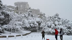 Des gens marchent dans la neige devant le temple du Parthénon au sommet de la colline de l'Acropole athénienne, à Athènes le 16 février 2021.