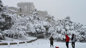 Des gens marchent dans la neige devant le temple du Parthénon au sommet de la colline de l'Acropole athénienne, à Athènes le 16 février 2021.