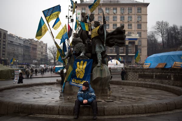 Un homme est assis sur une fontaine de la place Maïdan ornée d'une affiche du parti nationaliste ukrainien Svoboda et de drapeaux ukrainiens à Kiev, le 13 février 2014. 