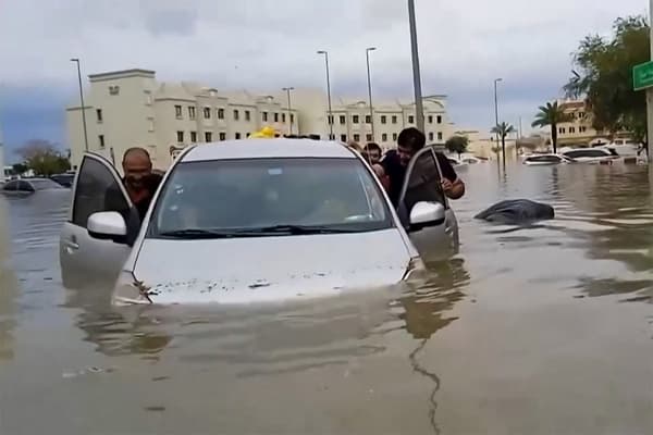 Des gens poussent une voiture bloquée dans une rue inondée à Dubaï le mardi 16 avril 2024. 