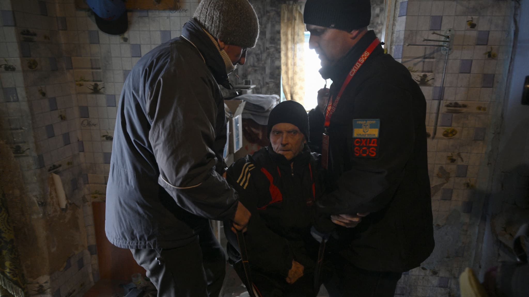 Deux hommes évacuent Volodymyr, 73 ans, de sa maison dans le village de Chernigivka, près de la ville de Pokrovsk dans la région de Donetsk (Ukraine), vers un véhicule d'évacuation de la Fondation SOS de l'Est, le 24 février 2025.