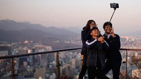 Des personnes utilisant une perche à selfie (ou selfie stick) depuis le toit d'un gratte-ciel de Séoul, en Corée du Sud. 