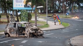 Un barrage et homme tenant un drapeau du Front de libération nationale kanak socialiste (FLNKS) dans le quartier N'Gea de Nouméa, le 14 mai 2024.