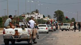 Insurgés libyens faisant route vers Tripoli, la capitale, dont les rebelles disent avoir pris plusieurs quartiers. La France a salué dimanche cette avancée et exhorté Mouammar Kadhafi et ses hommes à déposer les armes. /Photo prise le 21 août 2011/REUTERS