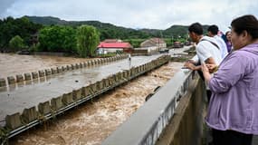 Des habitants observent les fortes pluies depuis un pont du village de Xin'anzhuang, dans le district de Miyun
