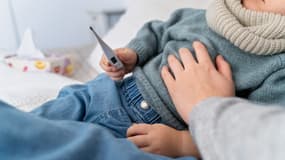 Un enfant malade tenant un thermomètre, avec sa mère à ses côtés (photo d'illustration)