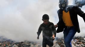 Un homme portant un masque à gaz escorte un enfant dans une rue enfumée d'Alep, en Syrie, le 24 mars 2013. (photo d'illustration)