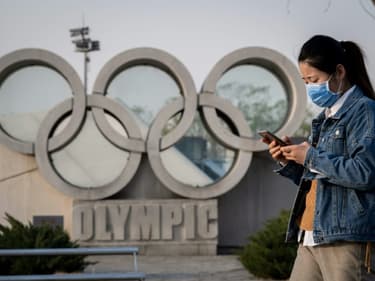 Une femme passe devant une sculpture représentant les anneaux olympiques, le 23 mars 2020 près du Stade National ou "Nid d'oiseau" à Pékin, où se dérouleront les Jeux olympiques (4 au 20 février 2022)