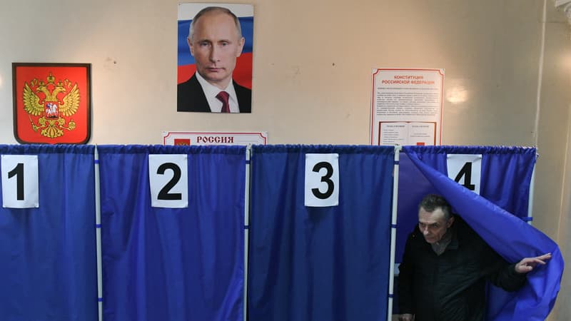 Un homme vote lors de l'élection présidentielle russe, sous un portrait de Vladimir Poutine, dans un bureau de vote à Donetsk, en Ukraine contrôlée par la Russie, le 16 mars 2024.