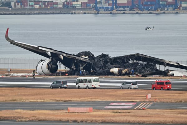 Des officiels regardent l'épave brûlée d'un avion de Japan Airlines sur le tarmac de l'aéroport international de Tokyo à Haneda à Tokyo le 3 janvier 2024, le matin après que l'avion ait percuté un plus petit avion des garde-côtes, faisant cinq morts.