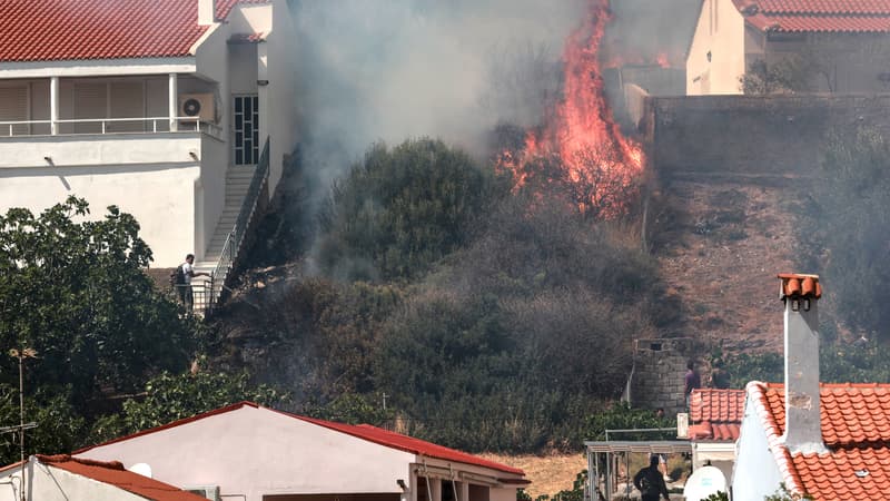 Des habitants regardent le feu qui brûle des arbres près des maisons de la station balnéaire de Vatera, sur l'île orientale de Lesbos, le 23 juillet 2022. Les résidents ont été évacués car le feu de forêt menaçait les propriétés.
