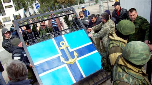 Derrière des militaires russes en faction, des militants pro-russes démontent et emportent la grille du siège de la marine ukrainienne à Sébastopol. Le bâtiment est contrôlé depuis quelques heures par l’armée russe.