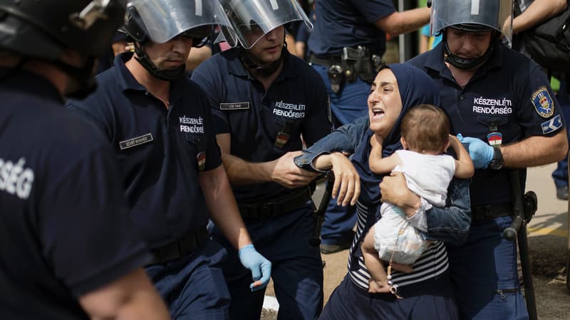 Une migrante cerclée de policiers tente de se débattre, son enfant dans les bras, le 3 septembre, à Bicske, en Hongrie. 