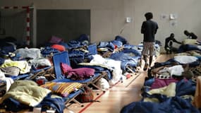 Un migrant marche entre des lits dressés dans un gymnase de l'université Panthéon-Assas, le 22 août 2017 à Paris. 