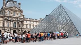 Des visiteurs faisant la queue devant la pyramide du Louvre.