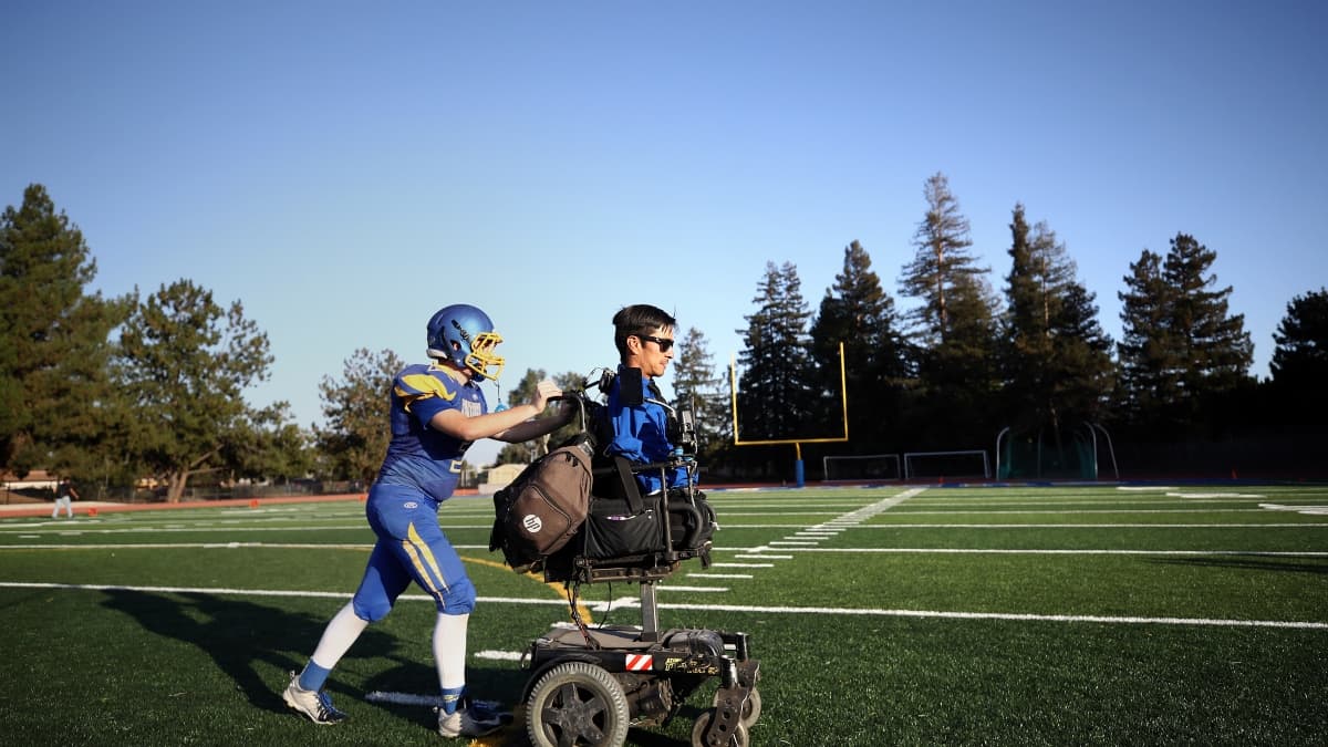 Rob Mendez poussé sur son fauteuil par un de ses joueurs de la Prospect High School lors de la saison 2018 Rob Mendez poussé sur son fauteuil par un de ses joueurs de la Prospect High School lors de la saison 2018