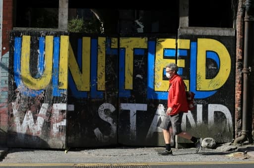 Un homme passe devant un message peint sur un mur "Nous restons unis", le 2 mai 2020 à Leeds, au Royaume-Uni