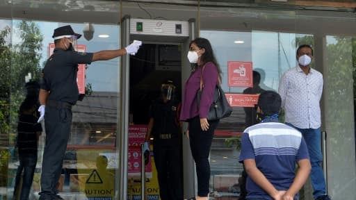 Un agent de sécurité prend la température d'une femme avant qu'elle entre dans un centre commercial, le 8 juin 2020 à Siliguri, en Inde