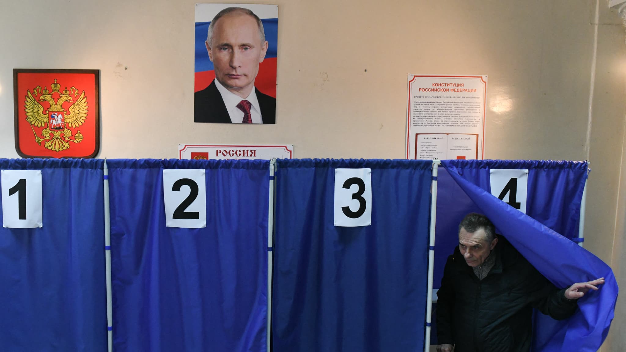 Un homme vote lors de l'élection présidentielle russe, sous un portrait de Vladimir Poutine, dans un bureau de vote à Donetsk, en Ukraine contrôlée par la Russie, le 16 mars 2024.