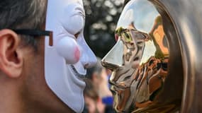 Un homme portant un masque de Guy Fawkes face à une statue en bronze en hommage à Satoshi Nakamoto, le pseudonyme du mystérieux inventeur de la cryptomonnaie Bitcoin, le 16 septembre 2021 à Budapest, en Hongrie
