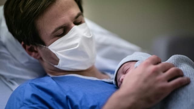 Un père portant un masque tient son bébé contre sa poitrine à la maternité des Diaconesses à Paris, le 17 novembre 2020