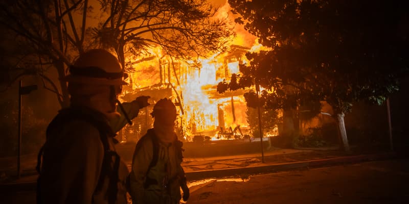 Un pompier passe devant une maison en flammes suite à l'incendie de Palisades lors d'une puissante tempête de vent le 8 janvier 2025 dans le quartier de Pacific Palisades à Los Angeles, en Californie.