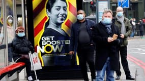 Des personnes portent un masque de protection à un arrêt de bus devant une affiche de campagne pour la 3e dose de vaccin contre le Covid-19, le 17 décembre 2021 à Londres