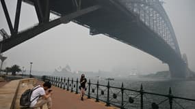 Des touristes avec des masques sous le pont de Harboug Bridge, entouré de la fumée causée par les feux de brousse, à Sydney le 10 décembre 2019