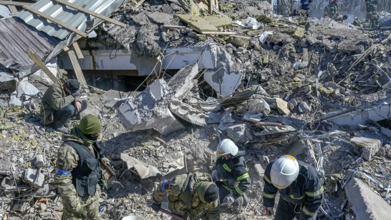 Des soldats ukrainiens et des équipes de secours cherchent des survivants dans les ruines  d'une caserne militaire touchée par des roquettes russes, à Mykolaïv, dans le sud de l'Ukraine, le 19 mars 2022

