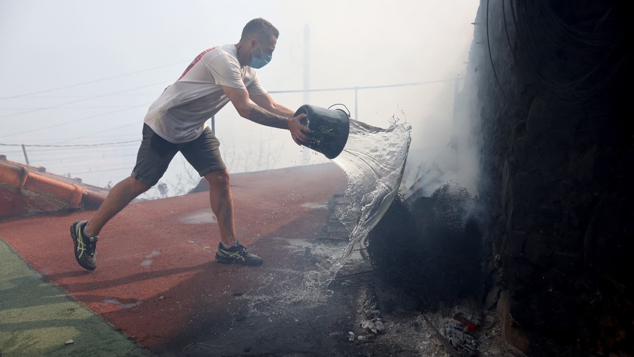 Un habitant tente d'éteindre un incendie près d'un mur lors d'un incendie de forêt qui se propage dans le quartier de l'Estaque à Marseille, dans le sud de la France, le 8 juillet 2025.