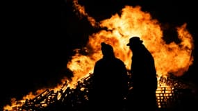 Deux agriculteurs devant un feu allumé lors d'un rassemblement contre la signature d'un accord de libre-échange entre l'Union européenne et des pays du Mercosur, à Dijon le 18 novembre 2024