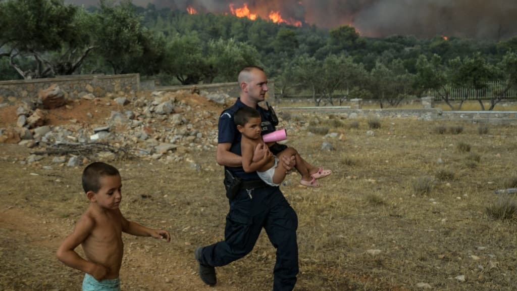 Un policier grec évacue un enfant d'un feu de forêt dans le village d'Agios Charamlabos, près d'Athènes, en Grèce, le 18 juillet 2023. Un policier grec évacue un enfant d'un feu de forêt dans le village d'Agios Charamlabos, près d'Athènes, en Grèce, le 18 juillet 2023.