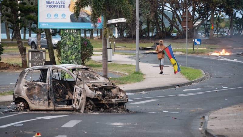 Un barrage et homme tenant un drapeau du Front de libération nationale kanak socialiste (FLNKS) dans le quartier N'Gea de Nouméa, le 14 mai 2024.