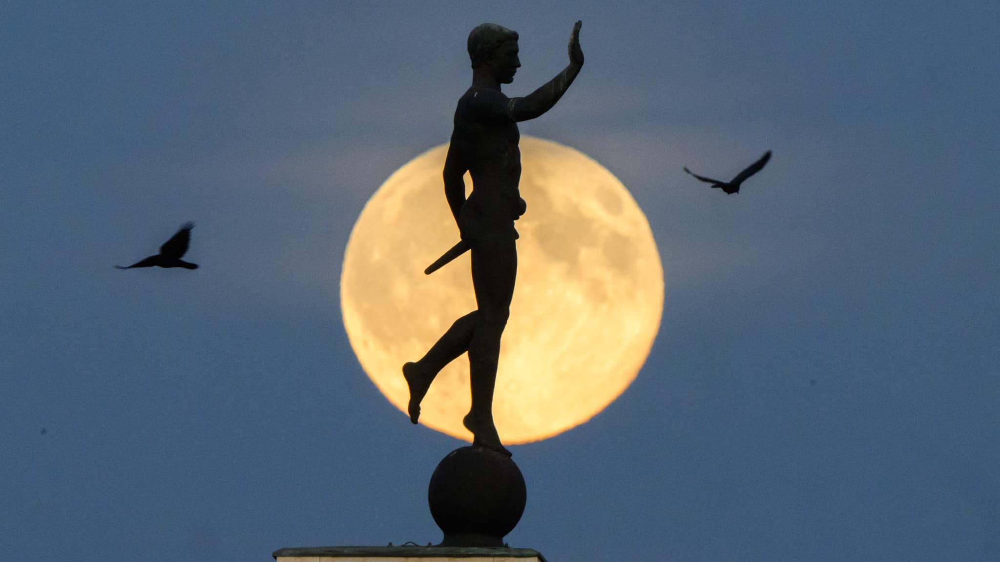 Суперлуна поднимается на горизонте за статуей.