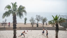 Des personnes jouent au volley-ball sur une plage alors que la poussière et le brouillard couvrent l'horizon dans la banlieue de Palaio Faliro, en Grèce, le 15 mars 2025.