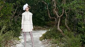 Pour l'été, les ensembles de tweed imaginés par Karl Lagerfeld pour Chanel scintillent de fil de métal, de boutons or ou argent, et se portent avec des jupes courtes ou mi-mollet, la jambe habillée de cuissardes de dentelle assorties, à bout ouvert. /Phot