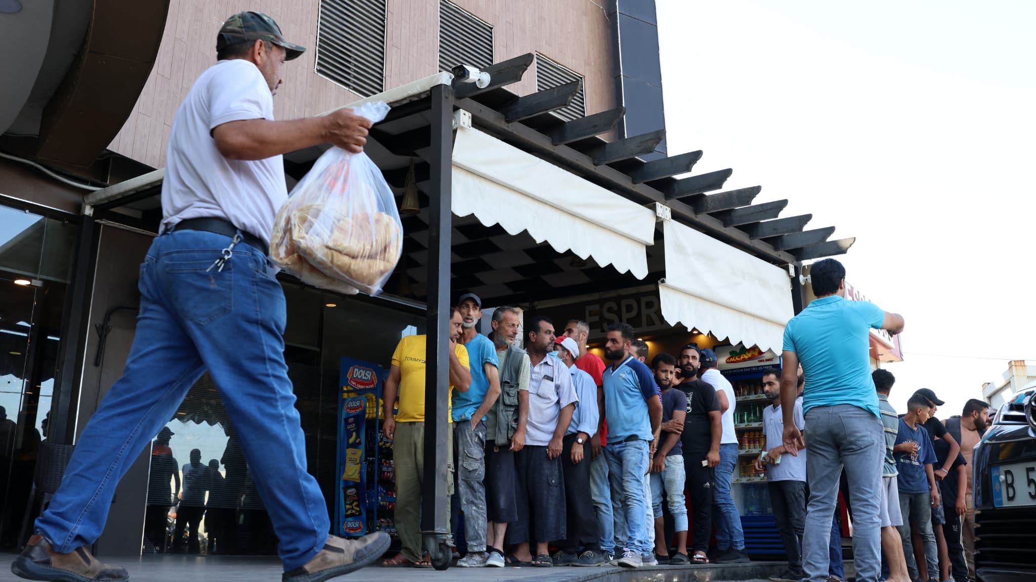 Un homme sort d'une boulangerie avec un sac de pain plat subventionné, alors que d'autres continuent à faire la queue, dans la capitale libanaise Beyrouth, le 29 juillet 2022, dans un contexte de pénurie d'approvisionnement en blé. 