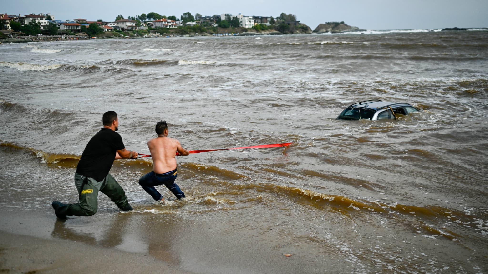 Des personnes tentent de sortir une voiture submergée par la mer au camping d'Arapia près de Tsarevo, sur la côte bulgare de la mer Noire, le 6 septembre 2023.