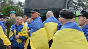 Des prisonniers de guerre ukrainiens enveloppés dans un drapeau national ukrainien à la suite d'un échange de prisonniers, dans un lieu inconnu, le 20 juin 2025.