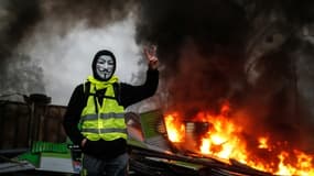 Un manifestant portant un gilet jaune et un masque près d'une barricade en feu