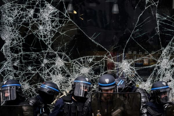 Des policiers devant la vitrine brisée d'un magasin pendant une manifestation contre la réforme des retraites, le 1er mai 2023 à Lyon