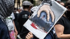 Une personne porte une pancarte lors d'une "Marche pour l'humanité" contre la crise humanitaire à Gaza, le 16 août 2025 à New York. Le dessin fait référence aux récents assassinats des journalistes d'Al Jazeera. 